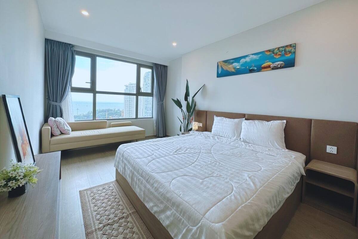 A modern bedroom with a large bed, a sofa, a window with a view, and a painting on the wall.