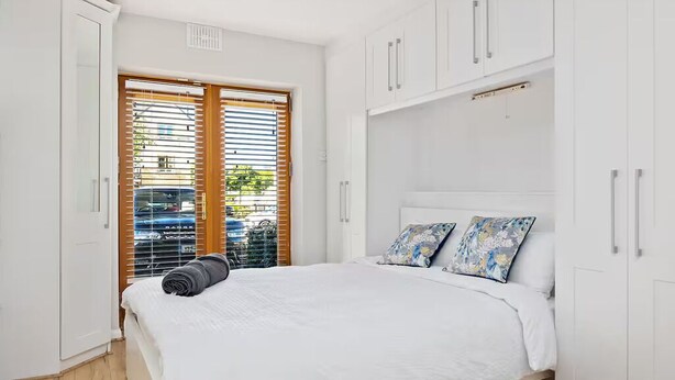 Un dormitorio con cama, armario blanco y ventana con persianas.