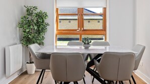 Un comedor con una mesa, cuatro sillas, una planta en maceta y una ventana que da a un edificio de ladrillo.
