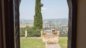 An arched doorway leading to a courtyard with a stone bench, potted plants, and a view of distant hills.