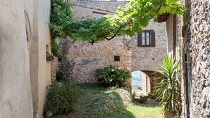 A narrow cobblestone path between buildings with stone walls and a vine-covered trellis.