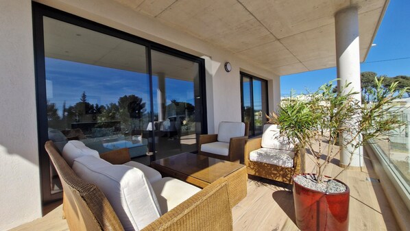 Relax in this serene outdoor seating area with sofas, chairs, and a coffee table, surrounded by lush greenery and a stunning view.