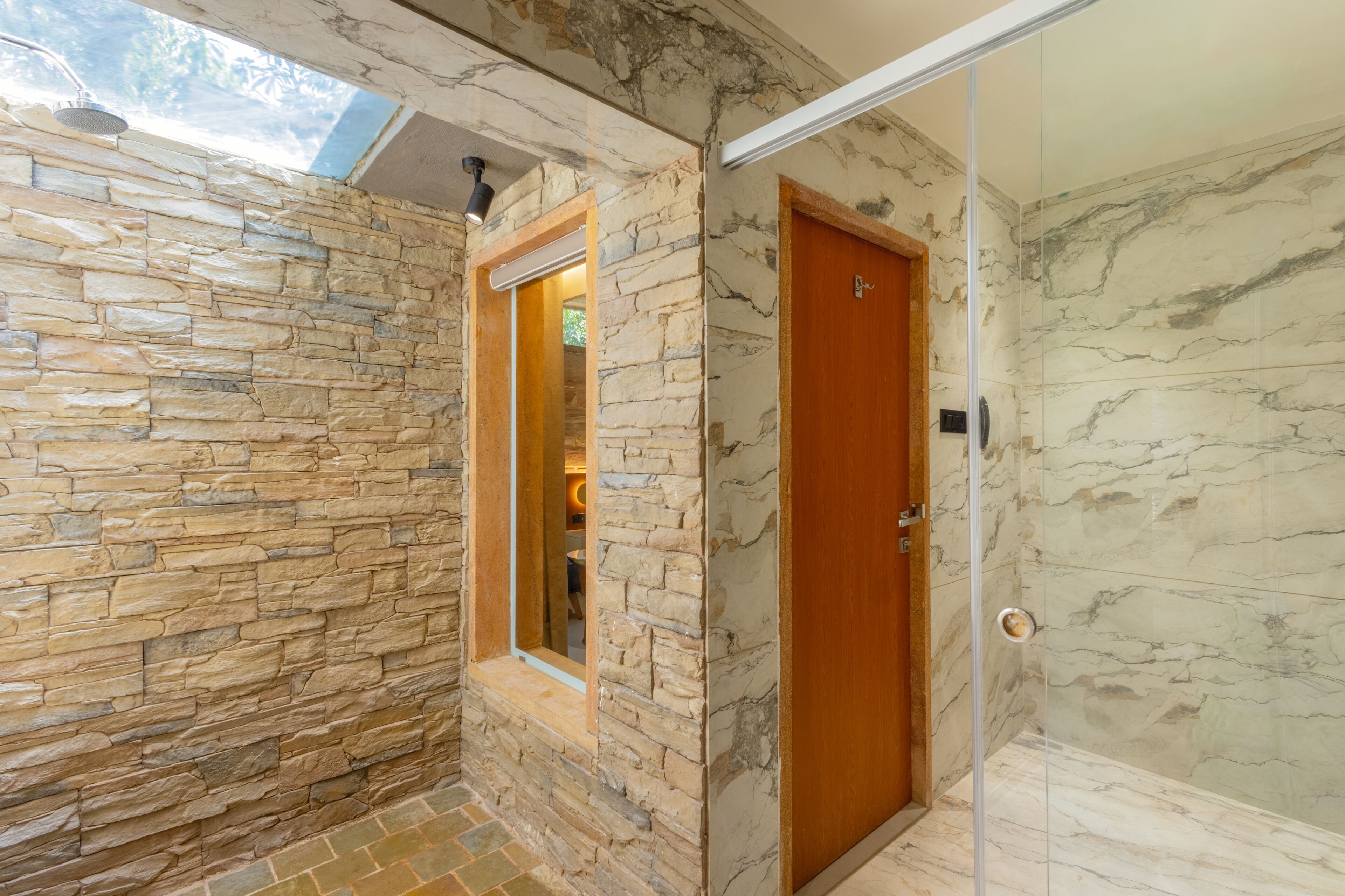A bathroom with stone walls, a wooden door, and a glass shower enclosure.
