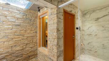 A bathroom with stone walls, a wooden door, and a glass shower enclosure.