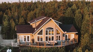 A large, multi-story cabin with a deck, surrounded by dense forest.