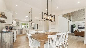 A modern kitchen with white cabinetry, a wooden dining table with white chairs, and pendant lighting.