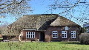 Une maison traditionnelle en briques, avec un toit de chaume, une porte d’entrée et un petit porche.