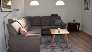 Un salon moderne avec un canapé d’angle, une petite table en bois et deux lampes fixées au mur.