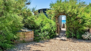 Ein Gartenweg führt zu einer Holzhütte mit Blick auf das Meer.