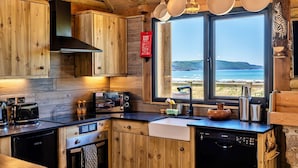 Eine Holzhüttenküche mit großem Fenster mit Blick auf einen Strand, einem Feuerlöscher und grundlegenden Küchengeräten.
