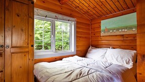 A wooden cabin bedroom with a bed, a window, and a painting on the wall. - Log Cabin in Snowdonia near Rhinog Mountains (Trawsfynydd)