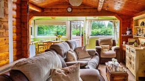 A cozy log cabin interior with a sofa, armchair, and wooden cabinets. - Log Cabin in Snowdonia near Rhinog Mountains (Trawsfynydd)