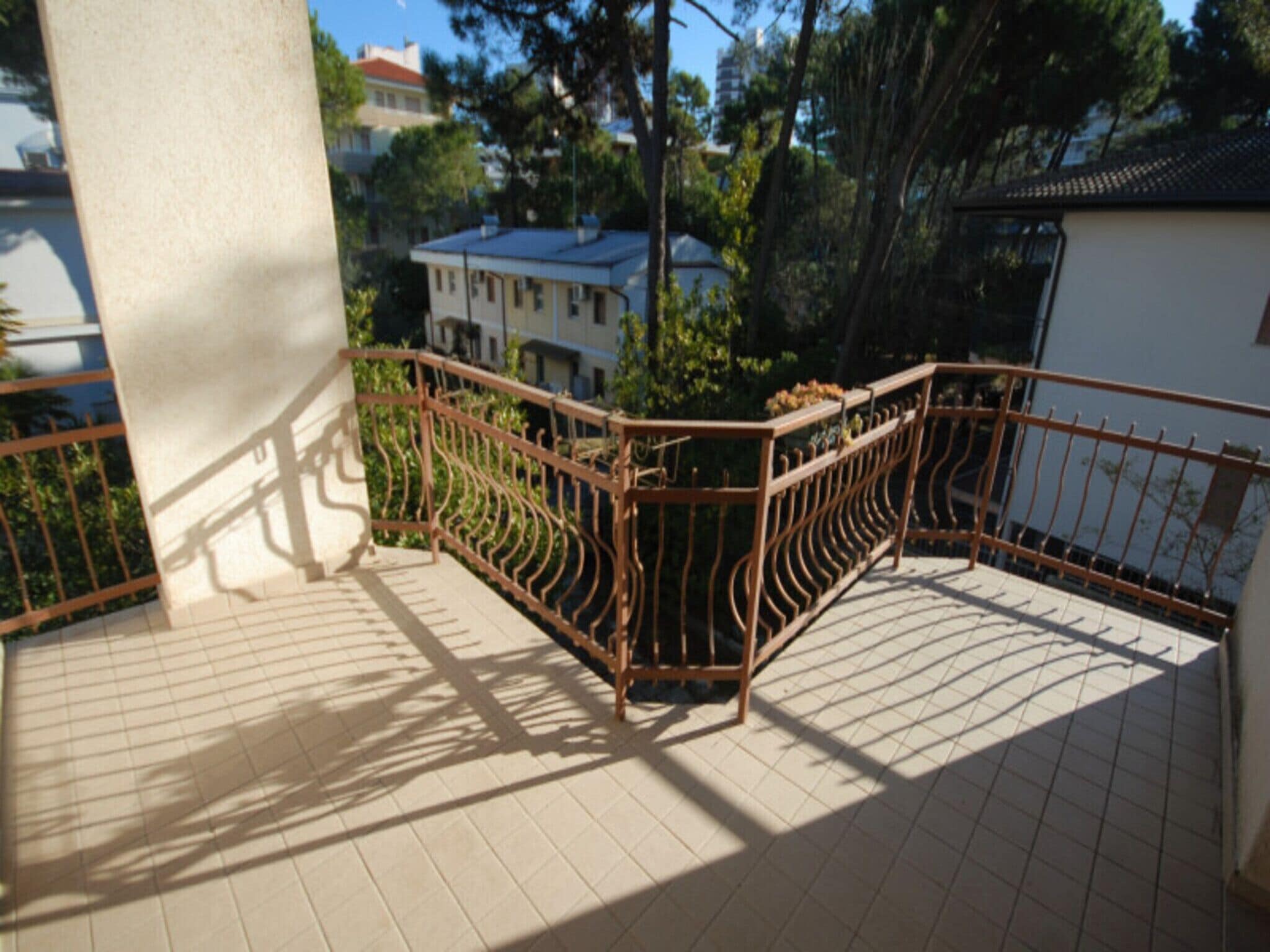 A balcony with a metal railing, tiled floor, and a view of buildings and trees in the background.