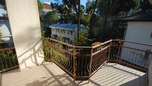 Un balcon doté d’une balustrade en métal, d’un sol carrelé et offrant une vue sur des bâtiments et des arbres en arrière-plan.
