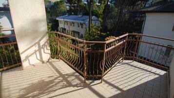 A balcony with a metal railing, tiled floor, and a view of buildings and trees in the background.