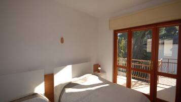 A bedroom with two beds, a nightstand, and a view of the outside balcony.
