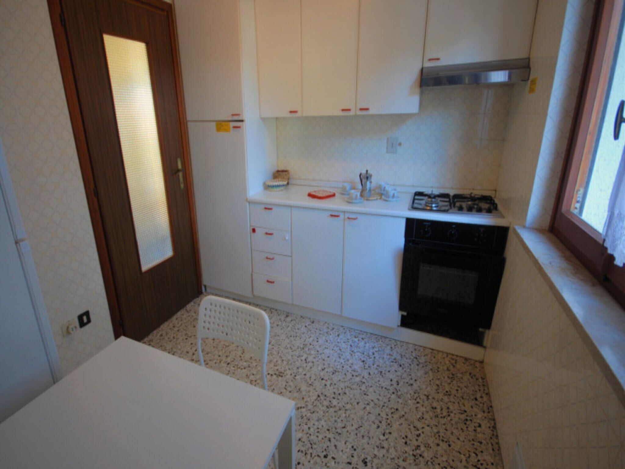 Une petite cuisine avec des armoires blanches, une cuisinière et un évier. On y trouve une chaise et une table.