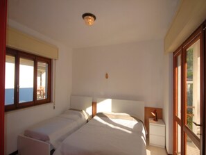 Un dormitorio con dos camas, una mesita de noche y una ventana con vista al mar.