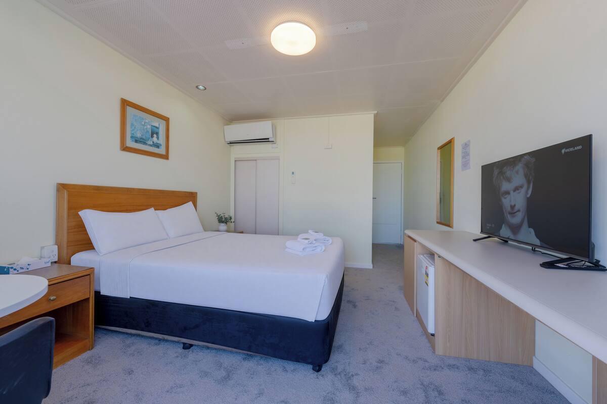A hotel room with a bed, a desk, a television, and a small kitchenette.