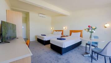 A hotel room with two beds, a desk, a chair, a small table, and a vase with flowers.