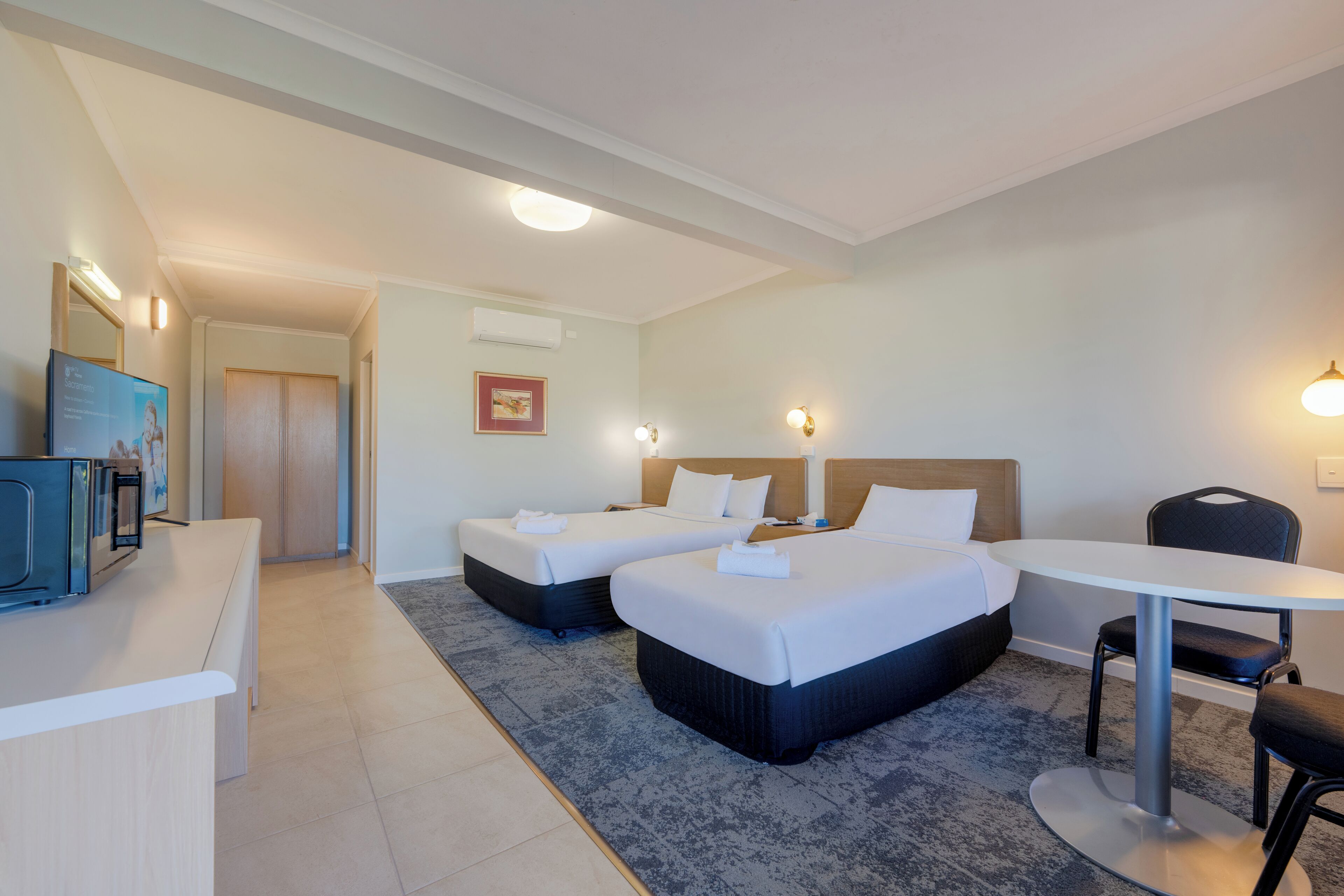 A hotel room with two beds, a desk, a chair, and a small table.