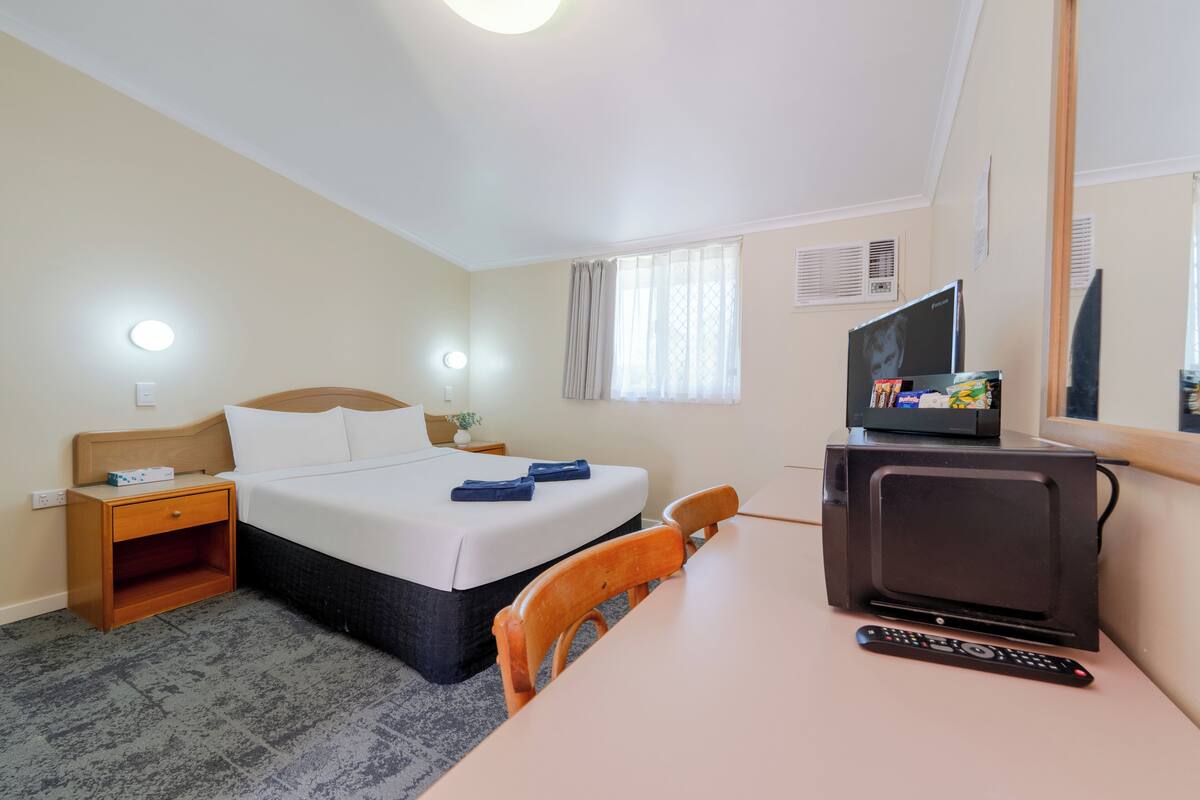 A hotel room with a bed, bedside table, TV, and a chair.