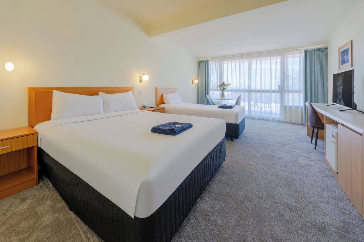 A hotel room with two beds, a desk, a chair, and a television.