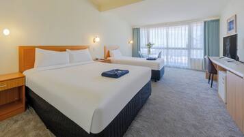 A hotel room with two beds, a desk, a chair, and a television.