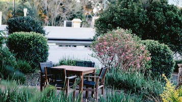 A patio with a wooden table and chairs, surrounded by lush greenery and a variety of plants.
