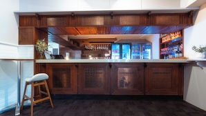 Una zona de bar con mostrador de madera, taburetes y vista a la cocina.