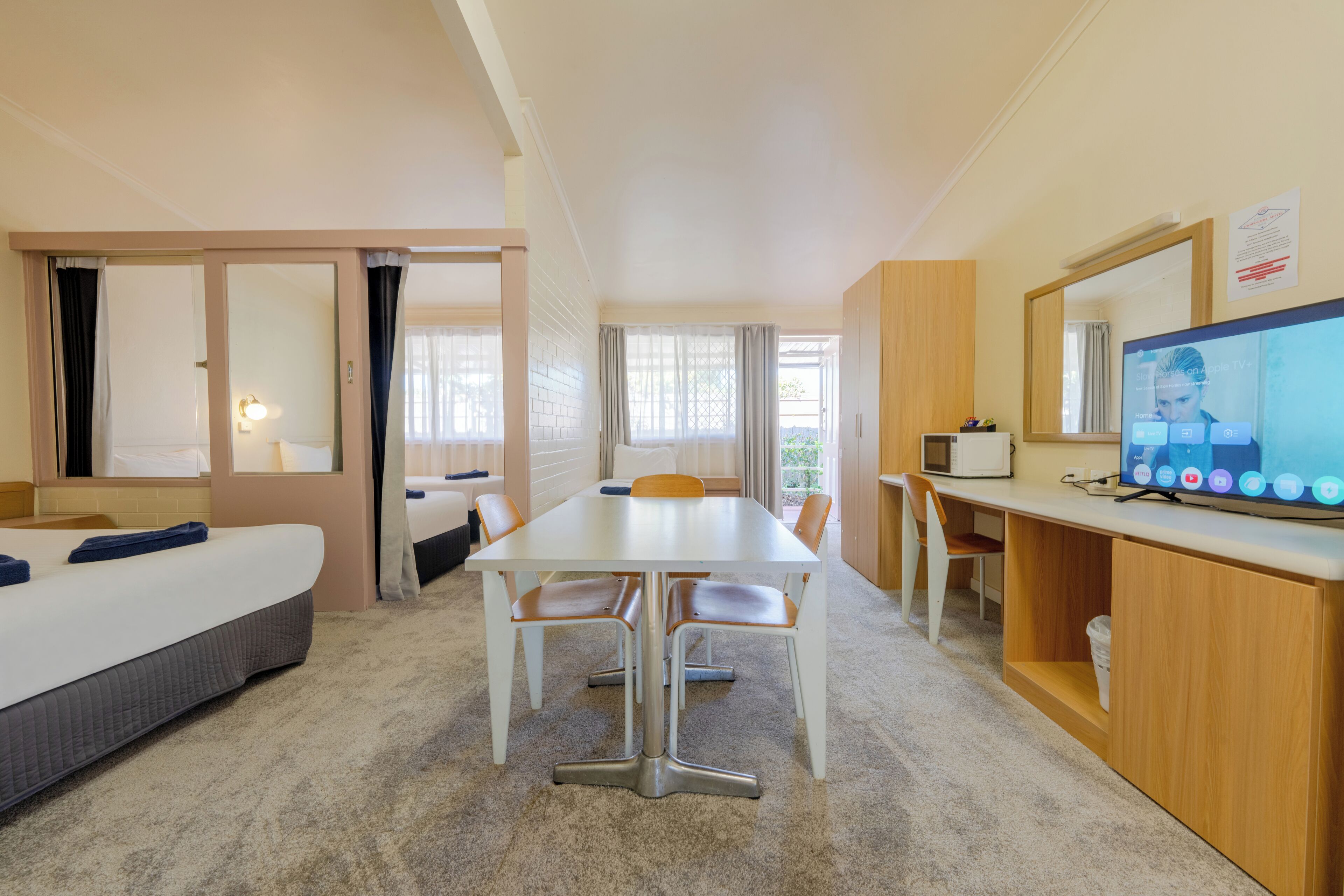 A hotel room with a bed, a dining table with chairs, a TV, and a small kitchenette.