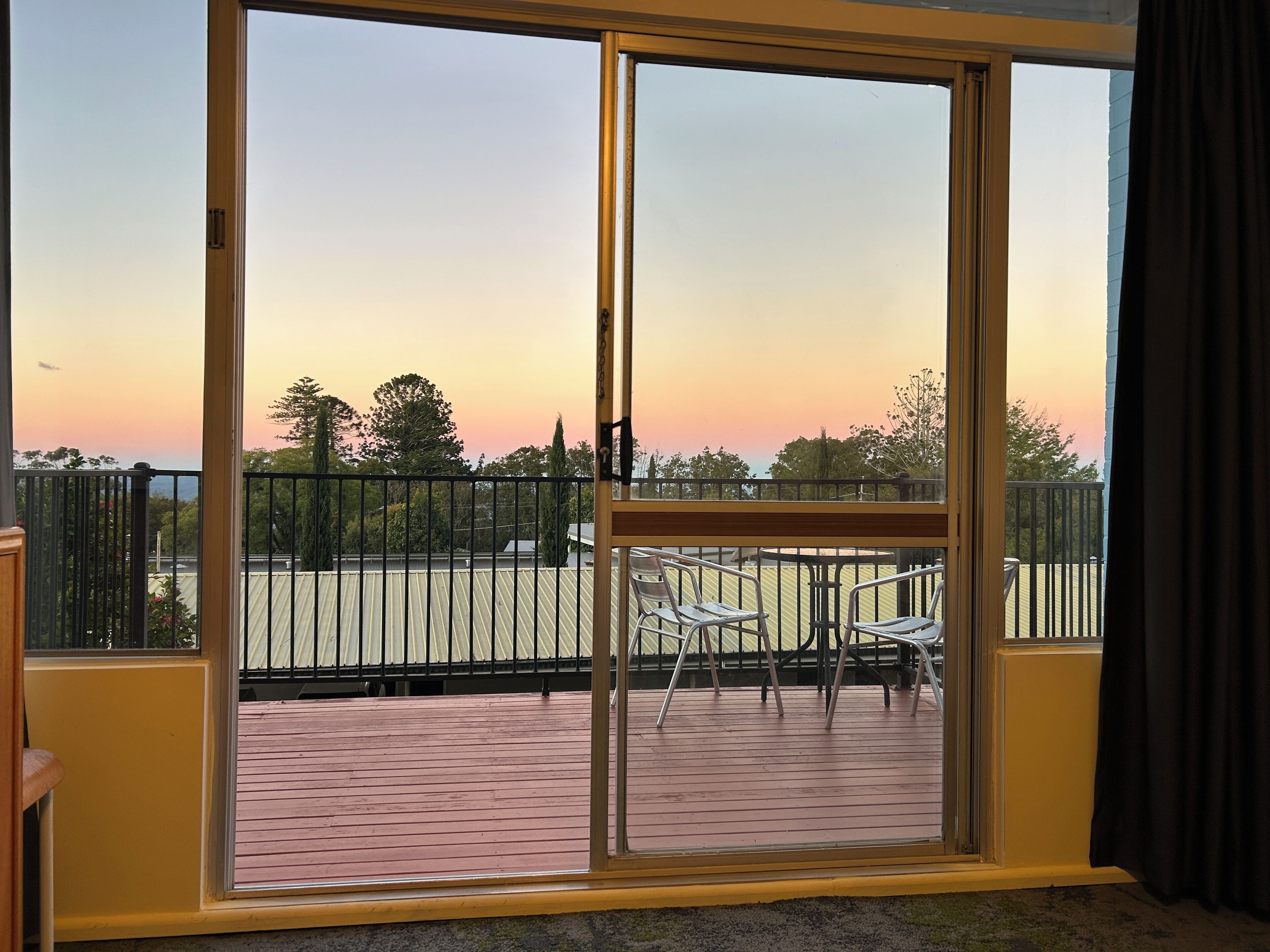 Un balcon avec vue sur le coucher de soleil, des chaises en métal et une rambarde.