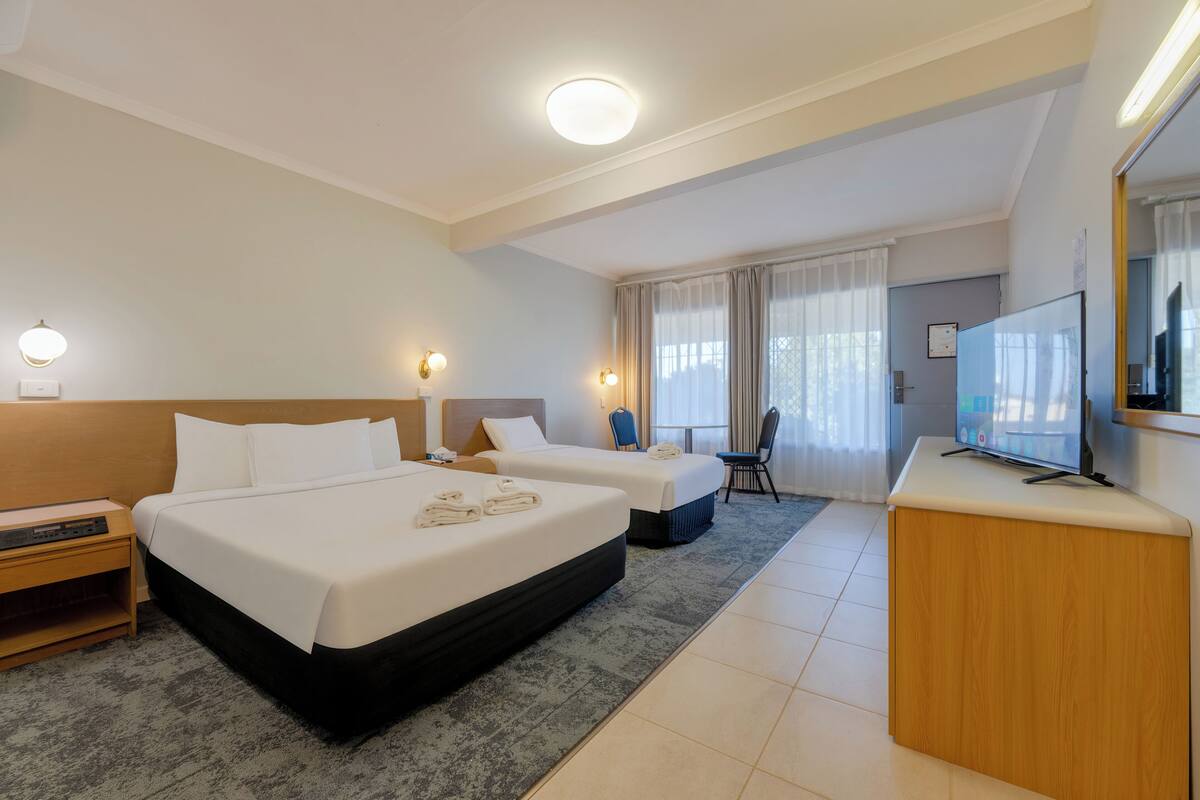 A hotel room with two beds, a desk, a TV, and a bathroom.