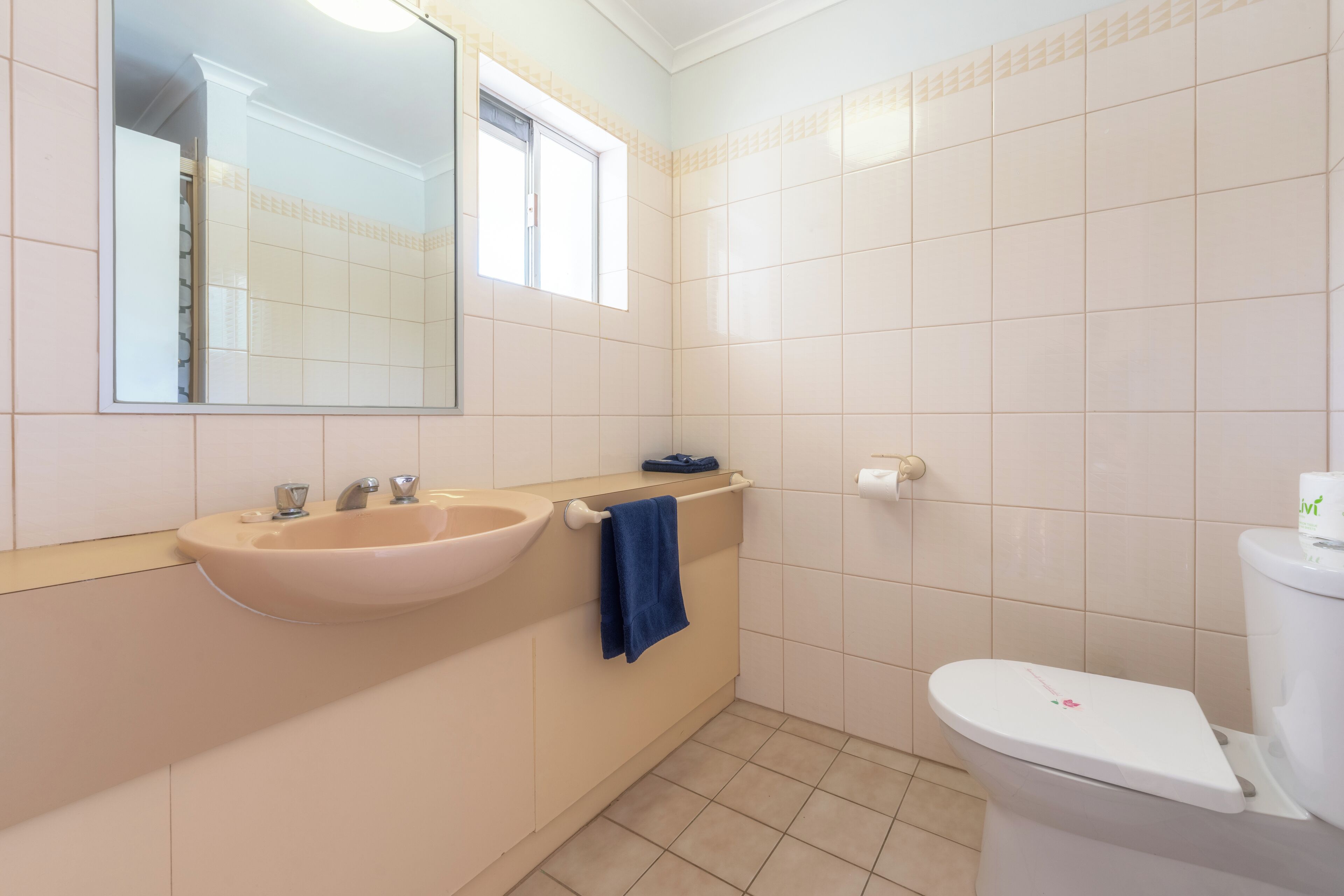 A bathroom with a sink, mirror, toilet, and a window.