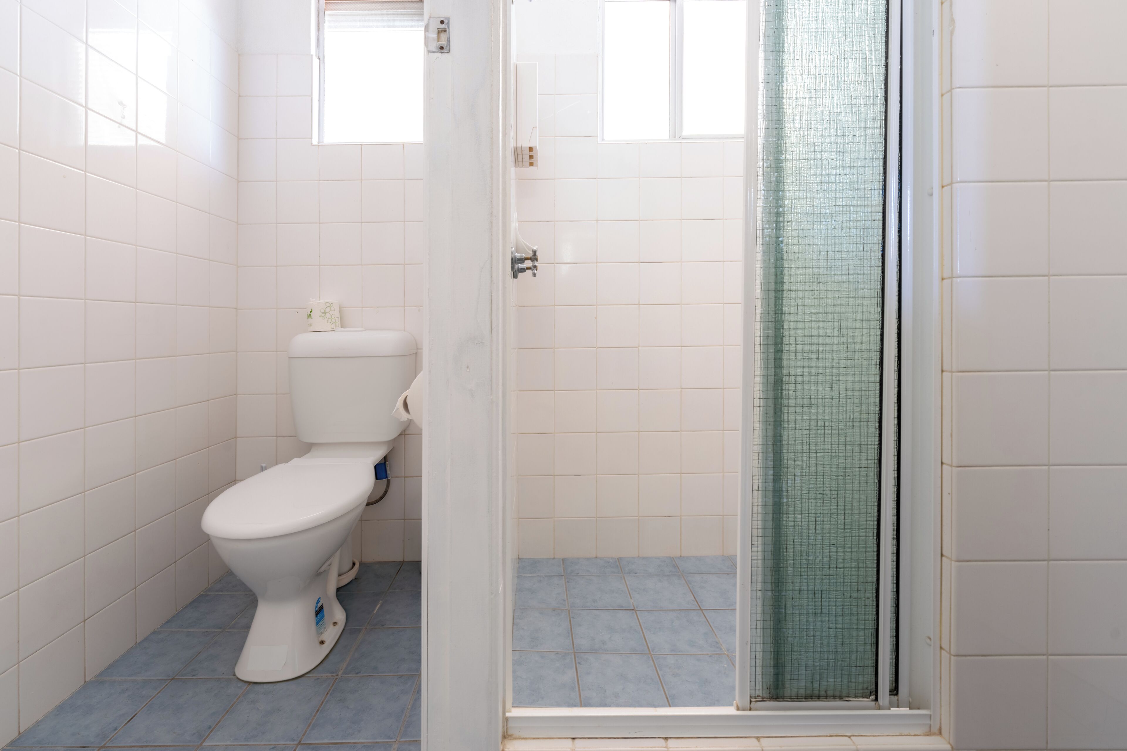 Ein Badezimmer mit Toilette, einer Dusche mit Glastür und gefliesten Wänden.