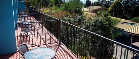 A balcony with a red wooden floor, metal railing, and two round tables with chairs.