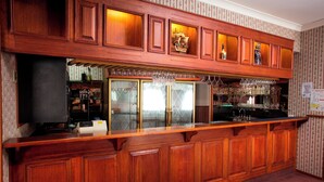 Una zona de bar con armarios de madera, un enfriador de vino y una variedad de copas.