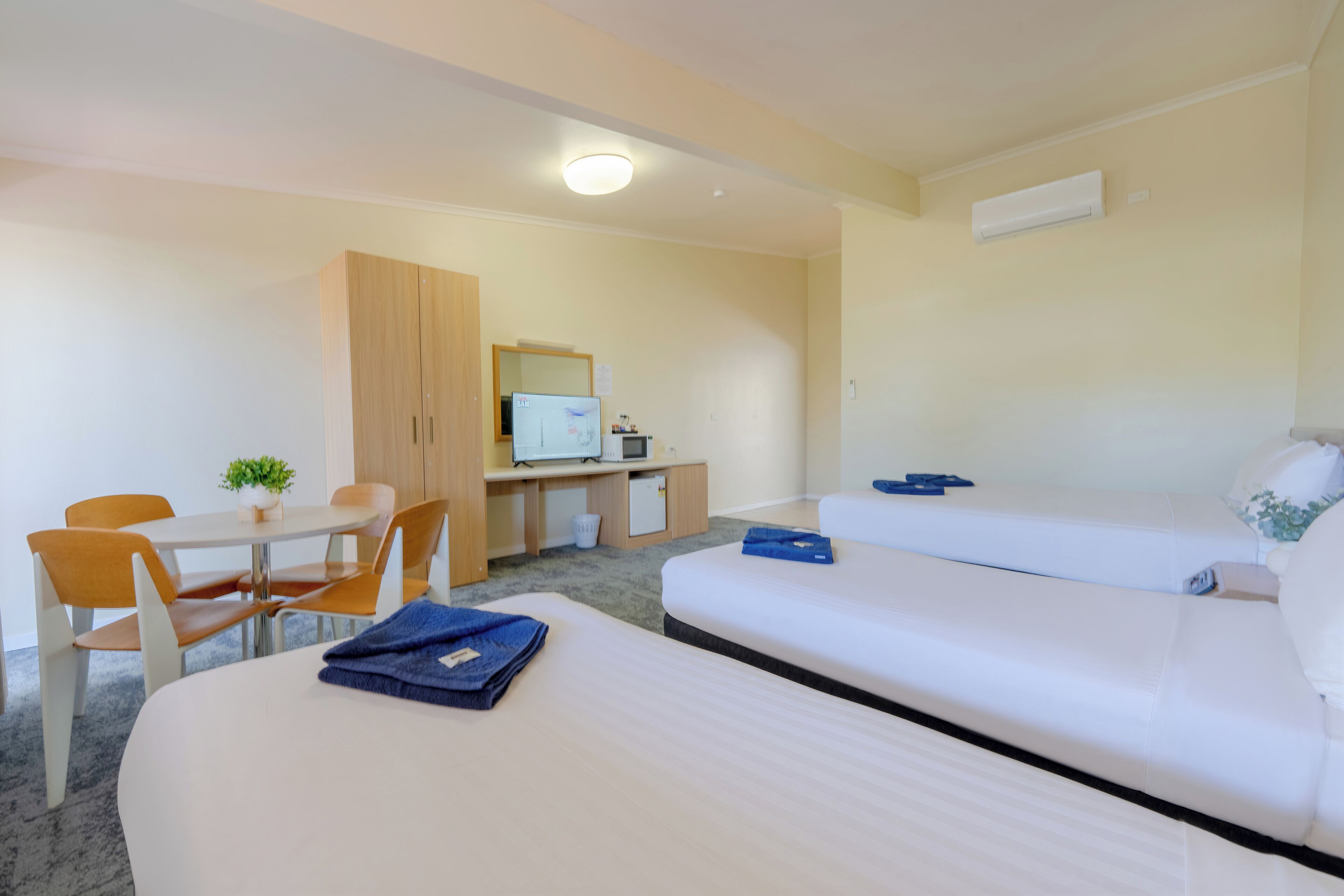 A hotel room with two beds, a desk with a computer, a chair, and a small table with a plant.