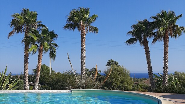 A pool with clear blue water, surrounded by palm trees and a view of the ocean. - The Wave, Sampieri, 2 minutes from the sea, villa with pool. (Sicilia)