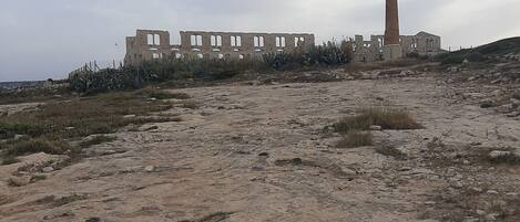 A historical site with ruins and a tall tower, featuring a rocky terrain and sparse vegetation.
