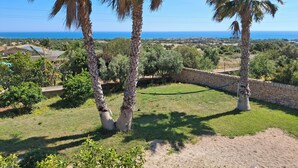 A view of a coastal landscape with palm trees, a stone wall, and a distant view of the sea. - The Wave, Sampieri, 2 minutes from the sea, villa with pool. (Sicilia)
