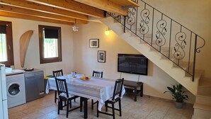 A dining area with a table set for four, a washing machine, a TV mounted on the wall, and a staircase with decorative railings. - The Wave, Sampieri, 2 minutes from the sea, villa with pool. (Sicilia)