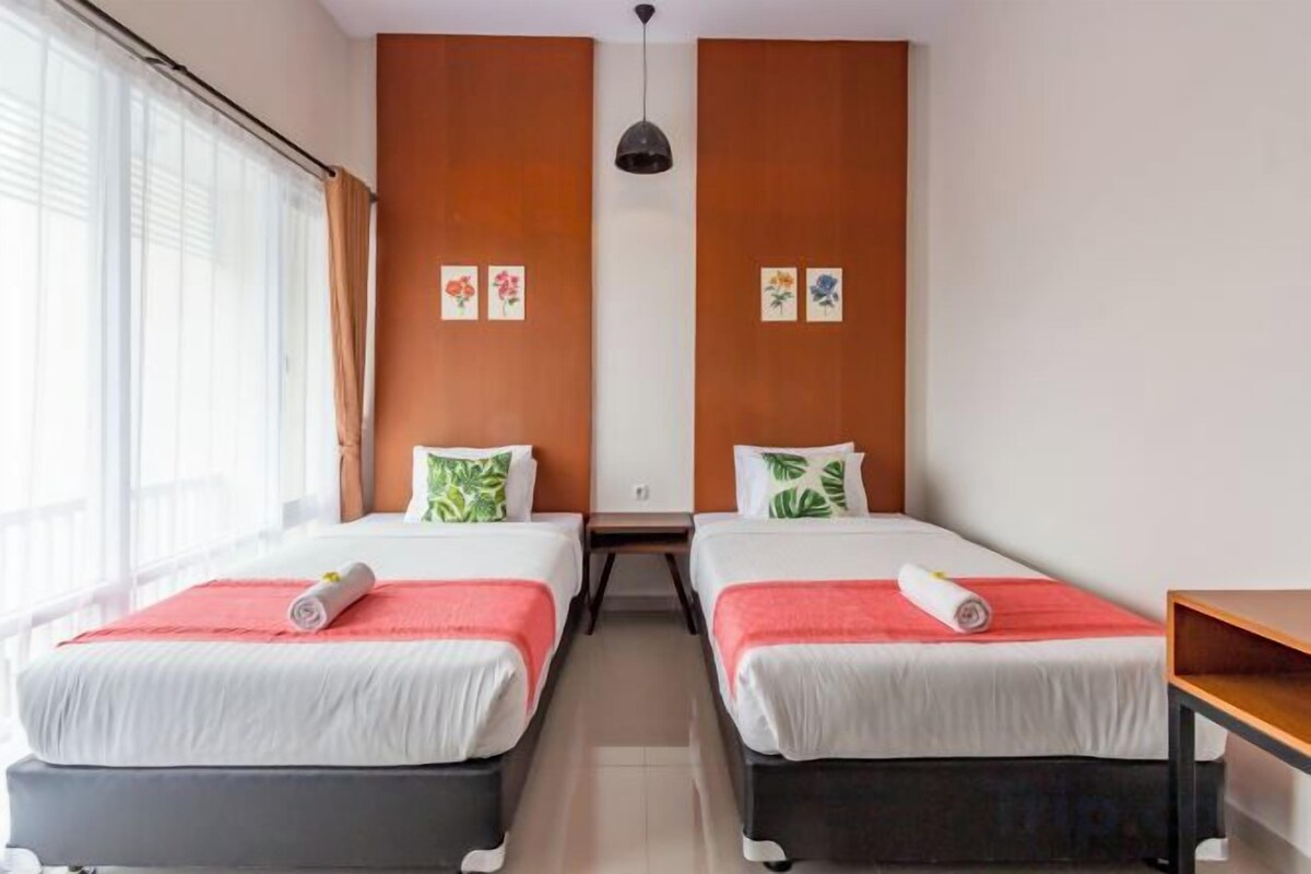 Habitación de hotel con dos camas, una mesita y un ventanal con cortinas.
