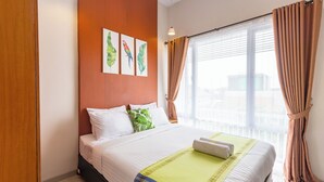 A hotel room with a bed, a window with curtains, and a wall with three framed pictures. - Omah Manis Taman Siswa (Yogyakarta)