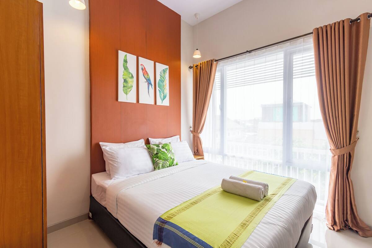 A hotel room with a bed, a window with curtains, and a wall with three framed pictures.