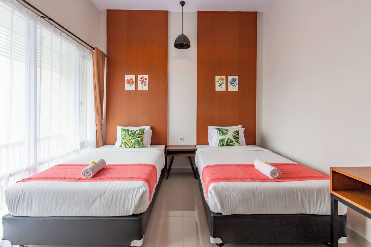 A hotel room with two beds, a wooden accent wall, a small table, and a window with curtains.