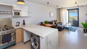 Moderni keittiö, jossa on sisäänrakennettu liesi, uuni ja pesukone, ruokailutila pöydän ja tuolien kera sekä näkymä suuresta liukuovesta ulos avautuvalle parvekkeelle.
