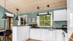 A modern kitchen with white cabinets, a central island, pendant lighting, and a view of greenery outside.