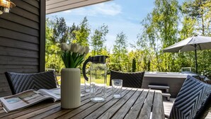 An outdoor patio with a wooden table, wicker chairs, a grill, and a view of trees.