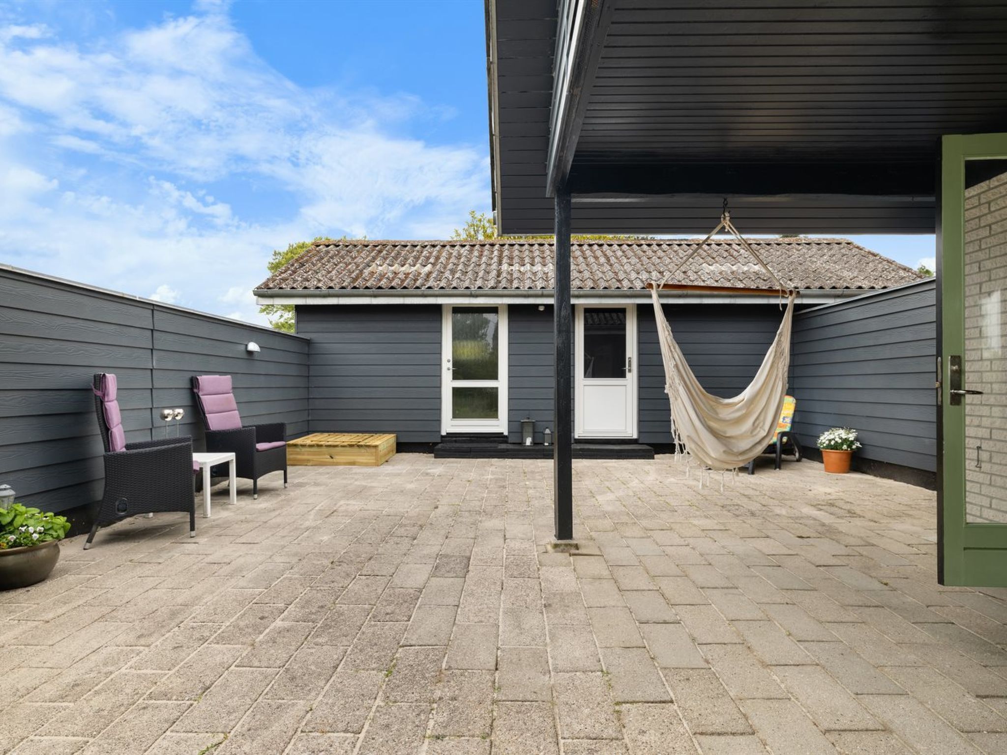 A covered patio with a hammock, outdoor furniture, and a small table.